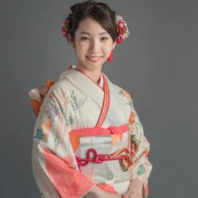 成人式撮影 H様 2021.05.09 御成町スタジオのグレー背景で、淡い水色とピンクの振袖を着て赤い髪飾りを付けた成人女性の上半身