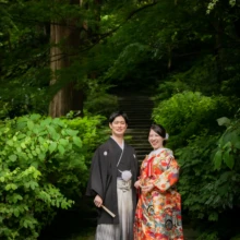 鎌倉 和装 I様・S様 2021.05.28 瑞泉寺の深い新緑を背景に、赤を基調とした色打掛の新婦と黒紋付袴の新郎が並んで微笑む鎌倉和装前撮り