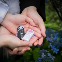 鎌倉 和装 I様・S様 2021.05.28 青い紫陽花を背景に、新郎新婦が手のひらへ載せた二つの小さな和装飾りを大きく捉えた記念カット
