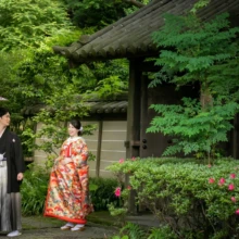鎌倉 和装 I様・S様 2021.05.28 瑞泉寺の木造建築と庭園を背景に、紫の和傘を持つ黒紋付袴の新郎と後ろ姿を見せる色打掛の新婦