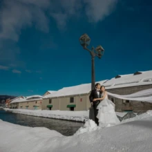 北海道 洋装 T様・T様 2022.02.07 深い雪と青空に囲まれた小樽の街で、街灯の下に寄り添って立つ新郎新婦の雪景色の洋装前撮り