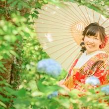 鎌倉 和装 M様・K様 2021.05.30 瑞泉寺の紫陽花と新緑を背景に、白い和傘を差した赤い色打掛姿の新婦が笑顔を見せる鎌倉和装前撮り