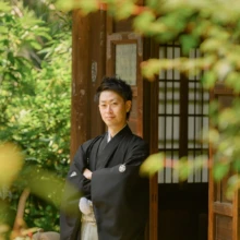 鎌倉 和装 M様・K様 2021.05.30 瑞泉寺の木造建築の入口で、黒紋付袴姿の新郎が腕を組んで立つ新緑に囲まれたソロカット