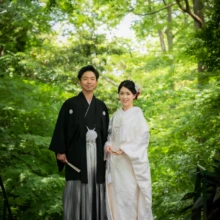 鎌倉 和装 O様・M様 2021.05.31 新緑が広がる妙本寺の境内で、髪飾りを付けた白無垢の新婦と黒紋付袴の新郎が並んで微笑む和装前撮り