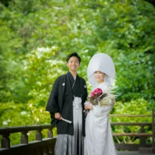 鎌倉 和装 O様・M様 2021.05.31 妙本寺の新緑に囲まれた高欄沿いで、花のブーケを持つ綿帽子と白無垢姿の新婦に黒紋付袴の新郎が寄り添う