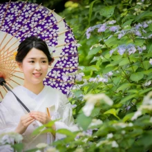 鎌倉 和装 O様・M様 2021.05.31 初夏の紫陽花と新緑に囲まれ、紫の和傘を差した白無垢姿の新婦が横を向く鎌倉和装前撮り