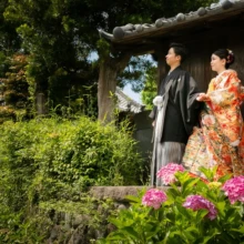 鎌倉 和装 O様・M様 2021.05.31 古い木造建築と鮮やかな紫陽花を背景に、華やかな色打掛の新婦と黒紋付袴の新郎が並ぶ鎌倉前撮り