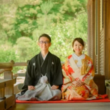 鎌倉 和装 M様・Y様 2021.06.01 建長寺の回廊に敷いた赤い毛氈に正座し、新緑を背に微笑む朱赤の色打掛の新婦と黒紋付袴の新郎