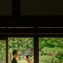 鎌倉 和装 M様・Y様 2021.06.01 建長寺の回廊で向かい合う色打掛の新婦と黒紋付袴の新郎を、緑を望む窓越しに捉えたシルエット