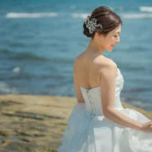 鎌倉 和洋装 H様・S様 2021.06.15 稲村ヶ崎の海と岩場を背景に、裾を広げたウェディングドレス姿で腰掛け、横顔を見せる新婦の鎌倉洋装前撮り