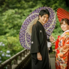 鎌倉 和装 T様・T様 2021.06.21 紫と赤の和傘を差し、妙本寺の廊下で振り返る黒紋付袴の新郎と朱赤の色打掛の新婦