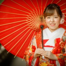 鎌倉 和装 T様・T様 2021.06.21 赤い和傘を背景に、鶴や花の文様が入った朱赤の色打掛姿で微笑む新婦の鎌倉和装前撮り