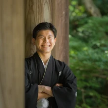 鎌倉 和装 M様・N様 2021.06.28 妙本寺の太い木柱の間で、黒紋付袴の新郎が腕を組んで笑顔を見せる鎌倉前撮りの新郎ソロカット