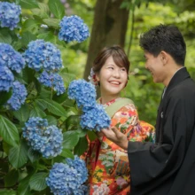 鎌倉 和装 M様・N様 2021.06.28 妙本寺の紫陽花のそばで、色打掛姿の新婦と黒紋付袴の新郎が花に手を添えながら笑い合う鎌倉和装前撮り