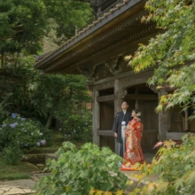 鎌倉 和装洋装 S様・S様 2021.06.25 英勝寺の木造建築と緑豊かな庭を広く背景に、朱赤の色打掛の新婦と黒紋付袴の新郎が並ぶ鎌倉和装前撮り