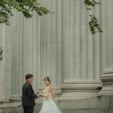 東京 洋装 T様・K様 2021.06.30 日本橋の円柱建築の前で、ロングトレーンのドレス姿の新婦とタキシードの新郎が手を取り合う東京フォトウェディング