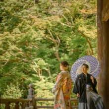 鎌倉 和装 S様・N様 2021.07.12 妙本寺の回廊で、淡い色打掛の新婦と紫色の和傘を差した黒紋付袴の新郎が向かい合う鎌倉和装前撮り