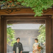 鎌倉 和装 S様・N様 2021.07.12 妙本寺の山門で、黒紋付袴の新郎と赤い裾が映える淡色の色打掛姿の新婦が和傘を足元に立つ鎌倉和装前撮り