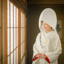 鎌倉 和装 N様・A様 2021.09.09 古民家スタジオの障子窓のそばで、綿帽子をかぶった白無垢姿の新婦が手を重ねて佇む鎌倉前撮り