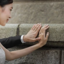 横浜 洋装 Y様・M様 2021.09.16 ウェディングドレス姿の新婦とタキシード姿の新郎が、馬車道の石壁に手を添えて指先を重ねる横浜前撮りのクローズアップ