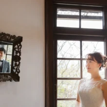 鎌倉 洋装 A様・I様 2020.11.12 洋館の窓辺に立つウェディングドレス姿の新婦と、壁の装飾鏡に映る黒いタキシード姿の新郎