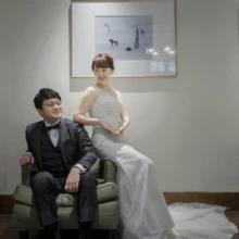 鎌倉 洋装 A様・I様 2020.11.12 洋館の室内で、緑色の椅子に座る黒いタキシード姿の新郎と、その肘掛けに腰掛けるウェディングドレス姿の新婦