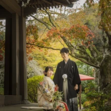 鎌倉 和装 S様・A様 2021.11.21 紅葉が見える寺院の縁側で、腰掛けた色打掛の新婦と隣に立つ黒紋付袴の新郎の鎌倉前撮り