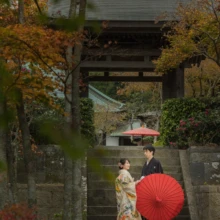 鎌倉 和装 S様・A様 2021.11.21 紅葉に囲まれた海蔵寺の山門の石段で、赤い和傘を添えて並ぶ色打掛の新婦と黒紋付袴の新郎