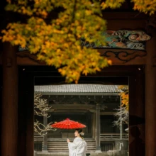 鎌倉 和装 A様・Y様 2021.12.07 晩秋の妙本寺で、紅葉に縁取られた門の奥に赤い和傘を背景に立つ白無垢姿の新婦の鎌倉前撮り