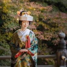 鎌倉 和装 T様・M様 2021.12.20 紅葉が残る妙本寺の橋で、両手を重ねて目を伏せる角隠しと緑の色打掛姿の新婦の鎌倉前撮り