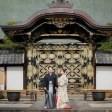 鎌倉 和装 M様・M様 2022.04.01 建長寺の金色装飾が施された唐門前で、向かい合って立つ淡い色打掛の新婦と黒紋付袴の新郎の鎌倉和装前撮り