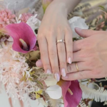 鎌倉横浜 和洋装 S様M様 2022.04.10 ピンクと紫のブーケの上に手を重ね、結婚指輪を見せるウェディングドレス姿の新婦と新郎の手元