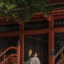 日光 和装 M様・M様 2022.08.29 奥日光の朱塗りの寺院の階段で、黒紋付姿の新郎と白無垢姿の新婦が並んで腰掛ける縦構図