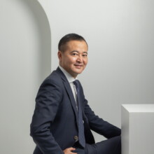 プロフィール写真 I様 2022.09.22 紺色のスーツとネクタイ姿の男性が、白い立体セットの中で横向きに腰掛けるビジネスプロフィール撮影