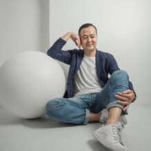 プロフィール写真 I様 2022.09.22 旧横浜店スタジオで、紺色のジャケットとデニム姿の男性が白い球体に囲まれ、床に座って笑うプロフィール撮影