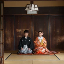 鎌倉 和装 K様・E様 2025.02.16 檑亭の和室で、赤い色打掛の新婦と黒紋付袴の新郎が、木製建具に囲まれた畳の上へ正座する