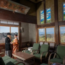 鎌倉 和装 K様・E様 2025.02.16 ステンドグラスと緑色の椅子が並ぶ檑亭の洋間で、色打掛の新婦と黒紋付袴の新郎が窓辺に立つ
