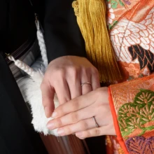鎌倉 和装 K様・E様 2025.02.16 金糸の刺繍が入った色打掛の袖と房飾りを背景に、新郎新婦が手を重ねた手元のクローズアップ