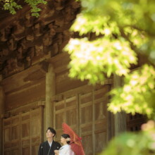 鎌倉 和洋装 K様・K様 2021.05.24 妙本寺の木造建築の回廊で、赤い和傘を差した白無垢の新婦と黒紋付袴の新郎が向かい合う鎌倉前撮り