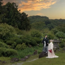 鎌倉 和装 O様・S様2026.06.26 夕焼け色の空と緑の山並みが広がる鎌倉・檑亭の庭園で、白無垢の花嫁と黒紋付の新郎が赤紫のブーケを手に並ぶ和装前撮り