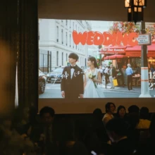 パリ 洋装 I様・I様 2025.09.17 結婚披露宴の会場で、パリのカフェを歩く新郎新婦の前撮り映像をスクリーンに上映し、ゲストが見守る様子