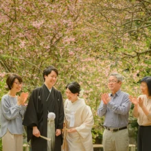 鎌倉和装 H様・H様 2021.03.29 満開の桜の下で、白無垢姿の新婦と黒紋付袴姿の新郎が家族に囲まれ、全員で笑顔を見せる記念撮影