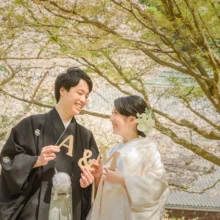 鎌倉和装 H様・H様 2021.03.29 妙本寺の桜を背景に、白無垢姿の新婦と黒紋付袴姿の新郎が木製のイニシャル小物を手に笑い合う和装前撮り