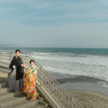 鎌倉和装 H様・H様 2021.03.29 鎌倉高校前の海岸を見渡す階段で、緑と赤の色打掛姿の新婦と黒紋付袴姿の新郎が手をつないで立つ
