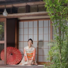 成人式撮影 M様 2023.08.09 鎌倉の古民家スタジオで、淡い桃色の振袖姿の女性が赤い和傘を添え、障子の前で正座する成人式撮影