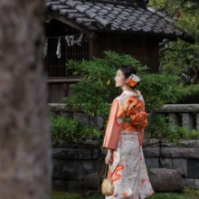 成人式撮影 M様 2023.08.09 夏の緑に囲まれた神社境内で、淡い桃色の振袖と金色の和装バッグを合わせた女性の成人式前撮り