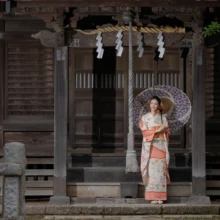 成人式撮影 M様 2023.08.09 鎌倉の神社拝殿を正面に、紫色の和傘を差して金色のバッグを持つ、淡い桃色の振袖姿の成人式撮影
