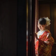 横浜 和装 Y様・O様 2022.04.14 山手西洋館の室内で、窓から差す光を受けながら赤い色打掛と白い髪飾りを見せる新婦の横顔