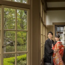 横浜 和装 Y様・O様 2022.04.14 庭園の新緑を望む山手西洋館の窓辺で、黒紋付の新郎と赤い色打掛の新婦が寄り添い見つめ合う姿