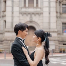 馬車道のクラシカルな街並みで見つめ合う、ブラックドレスが映えるウェディングフォト|縁グラフィの姉妹ブランドLuca 横浜・馬車道のクラシカルな歴史的建築を背景に、ブラックドレス姿の花嫁とタキシード姿の新郎が見つめ合うウェディングフォト